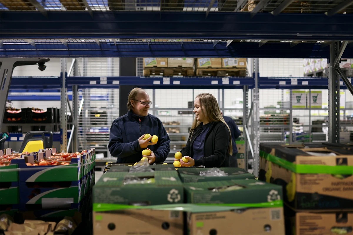 Två glada lagerarbetare som plockar frukt och grönt.