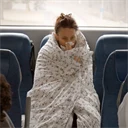 Förkyld kvinna invirad i täcke på bussen på väg till jobbet.